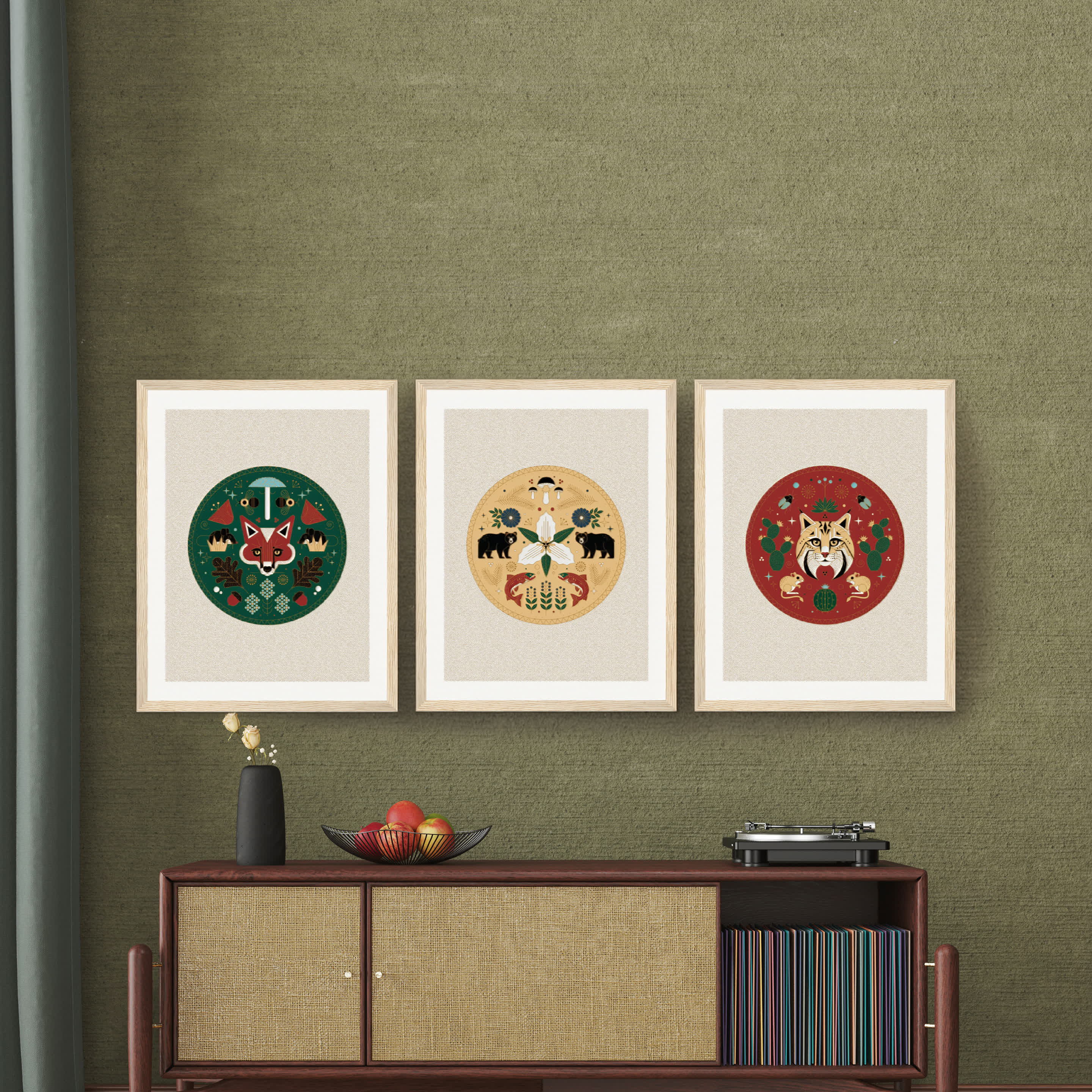 Three framed animal-themed artworks on a green wall above a mid-century modern console with decor.